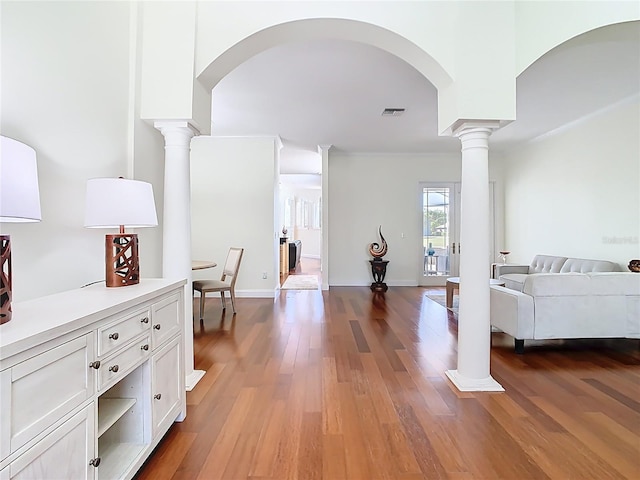 hall featuring wood finished floors, decorative columns, arched walkways, and visible vents