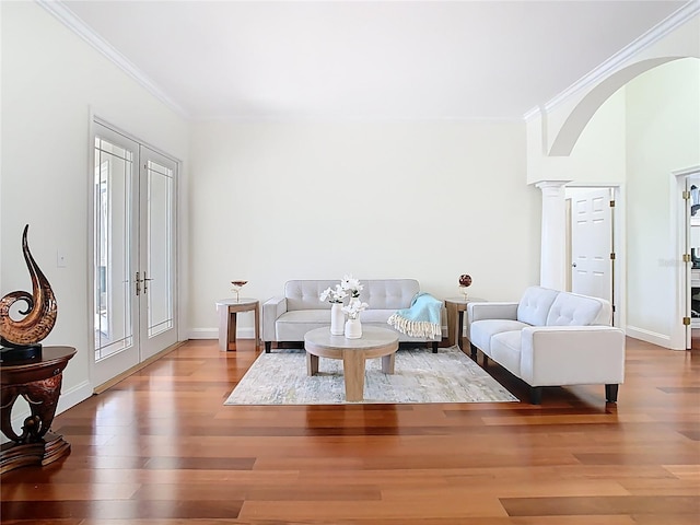 living area with arched walkways, ornamental molding, and wood finished floors