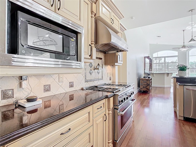 kitchen with wood finished floors, under cabinet range hood, appliances with stainless steel finishes, dark countertops, and cream cabinets