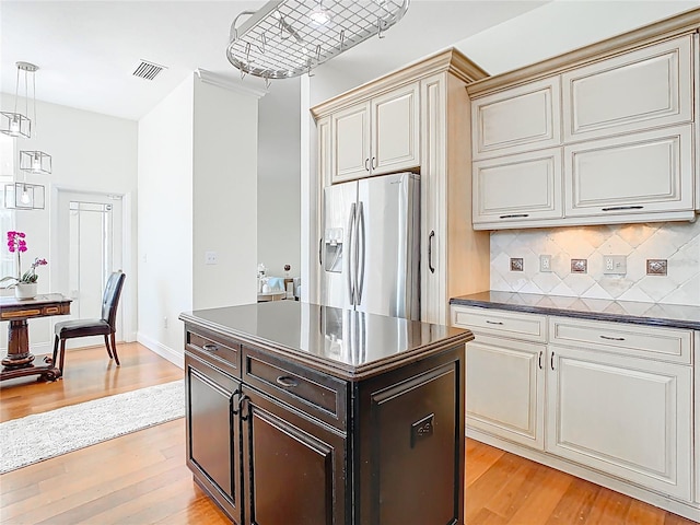 kitchen with light wood-style flooring, stainless steel refrigerator with ice dispenser, dark countertops, decorative backsplash, and hanging light fixtures