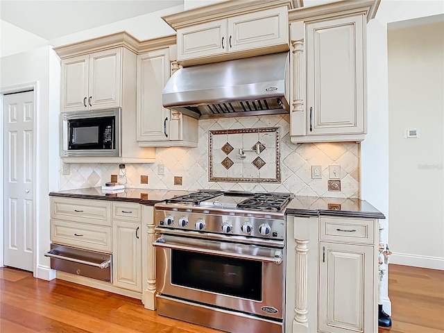 kitchen with a warming drawer, under cabinet range hood, dark countertops, built in microwave, and high end range