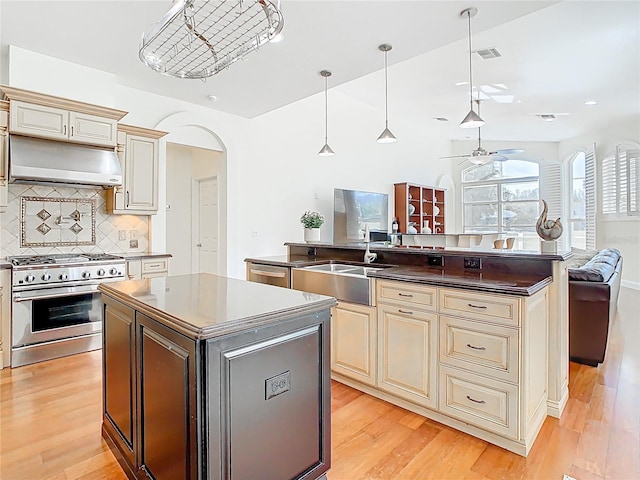 kitchen featuring under cabinet range hood, high end range, cream cabinetry, and a center island