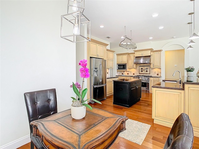 kitchen featuring a kitchen island, a sink, cream cabinetry, under cabinet range hood, and appliances with stainless steel finishes