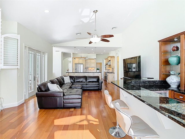 living area featuring visible vents, high vaulted ceiling, light wood-type flooring, and a ceiling fan