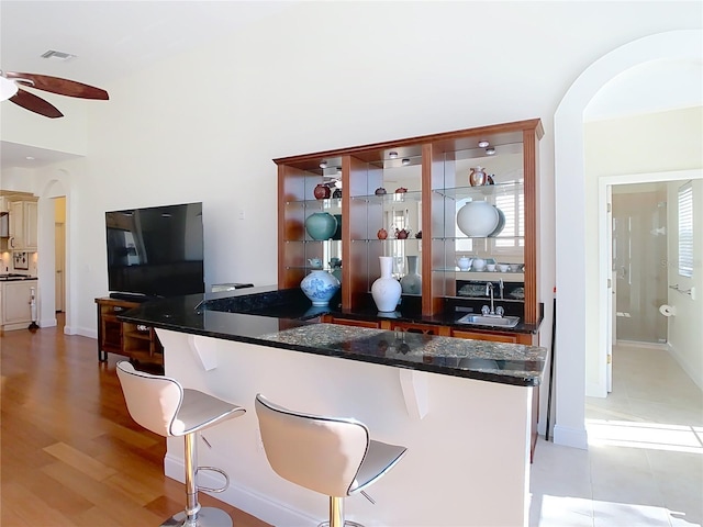 kitchen with a breakfast bar area, light wood-style flooring, arched walkways, ceiling fan, and a sink