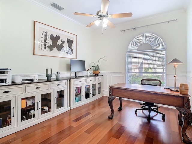 home office with visible vents, ornamental molding, a ceiling fan, wood finished floors, and wainscoting