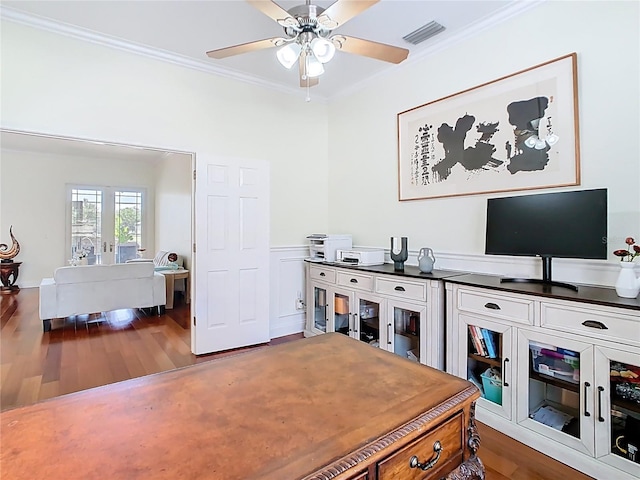 home office with dark wood-style floors, a wainscoted wall, visible vents, ceiling fan, and ornamental molding