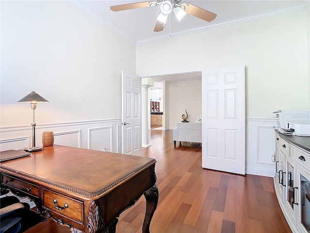 office with crown molding, ceiling fan, a wainscoted wall, decorative columns, and dark wood-style flooring