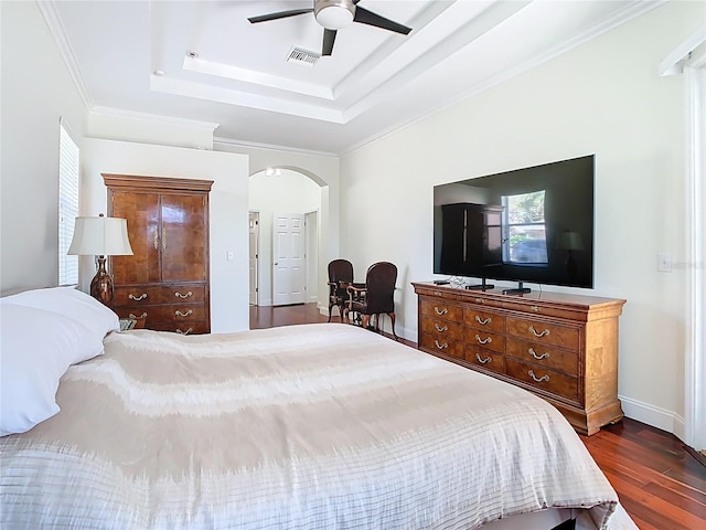 bedroom featuring visible vents, crown molding, dark wood finished floors, a tray ceiling, and arched walkways