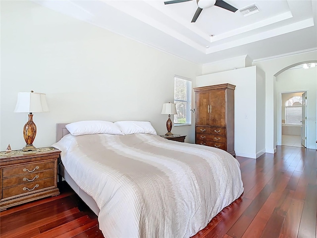 bedroom with visible vents, hardwood / wood-style flooring, arched walkways, a raised ceiling, and a ceiling fan