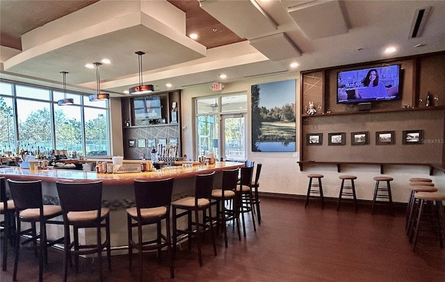 bar with baseboards, a tray ceiling, indoor wet bar, dark wood-type flooring, and backsplash