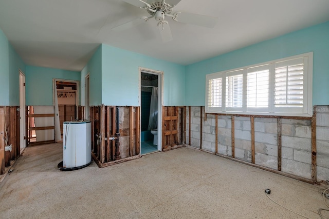 unfurnished bedroom with wainscoting, gas water heater, connected bathroom, and a ceiling fan