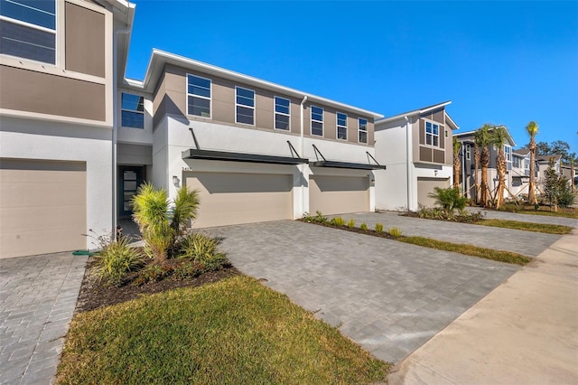 view of property with a residential view, decorative driveway, an attached garage, and stucco siding