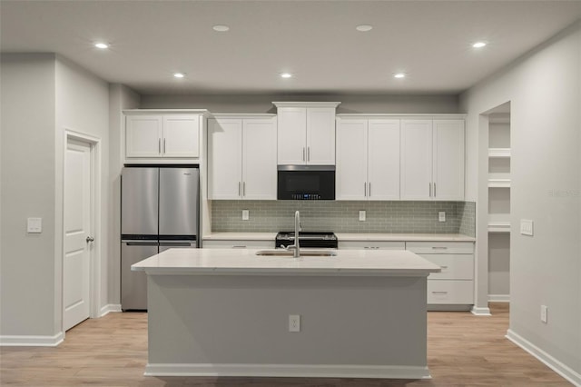 kitchen featuring a sink, white cabinets, freestanding refrigerator, light wood finished floors, and an island with sink