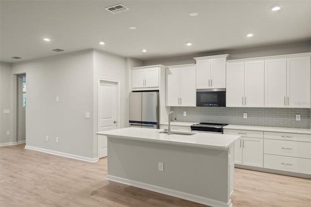 kitchen with visible vents, a kitchen island with sink, stainless steel appliances, white cabinetry, and a sink