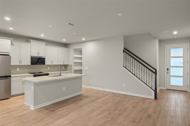 kitchen featuring a center island with sink, white cabinets, stainless steel appliances, light countertops, and a sink