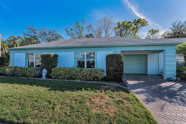 ranch-style house with decorative driveway, stucco siding, an attached garage, and a front yard