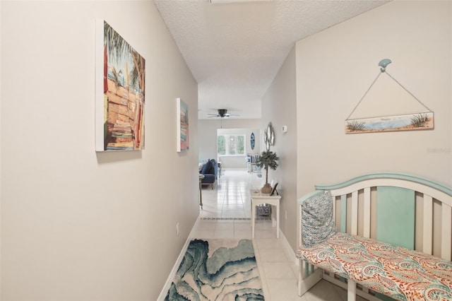 hallway with a textured ceiling, baseboards, and tile patterned floors