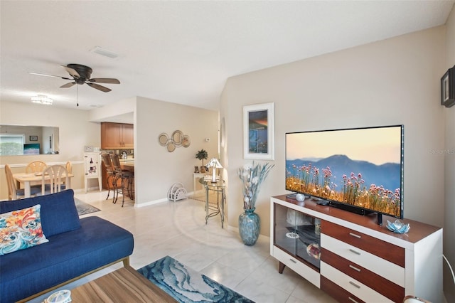 living area with visible vents, ceiling fan, baseboards, and light tile patterned floors