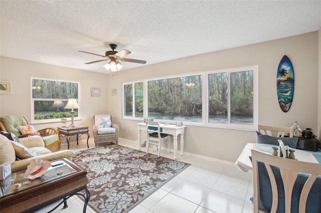 living area featuring ceiling fan, a textured ceiling, tile patterned flooring, and baseboards