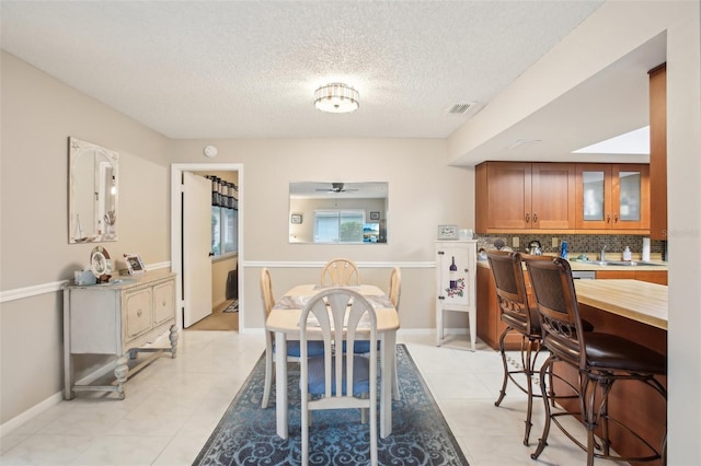 dining space featuring light tile patterned floors, visible vents, ceiling fan, a textured ceiling, and baseboards