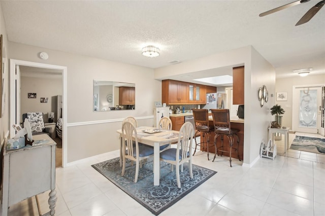 dining space with ceiling fan, a textured ceiling, baseboards, and light tile patterned floors