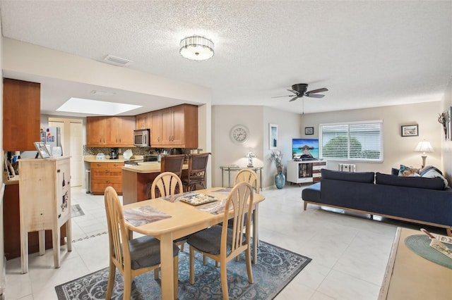 dining space with a skylight, visible vents, a ceiling fan, light tile patterned flooring, and a textured ceiling