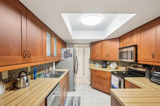 kitchen with a sink, appliances with stainless steel finishes, decorative backsplash, a raised ceiling, and glass insert cabinets