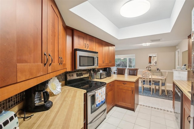 kitchen featuring tasteful backsplash, a raised ceiling, wood counters, appliances with stainless steel finishes, and brown cabinets