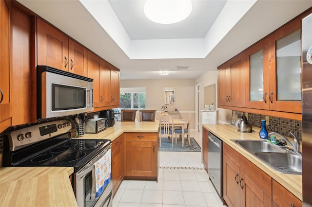 kitchen with stainless steel appliances, a raised ceiling, backsplash, glass insert cabinets, and a sink