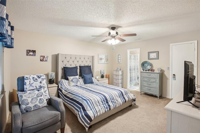 bedroom with light carpet, ceiling fan, a textured ceiling, and connected bathroom