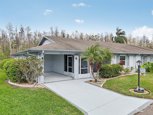 ranch-style home with driveway, roof with shingles, a front lawn, a carport, and stucco siding