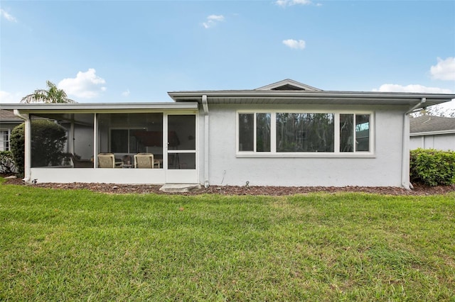 rear view of house with a sunroom, a lawn, and stucco siding