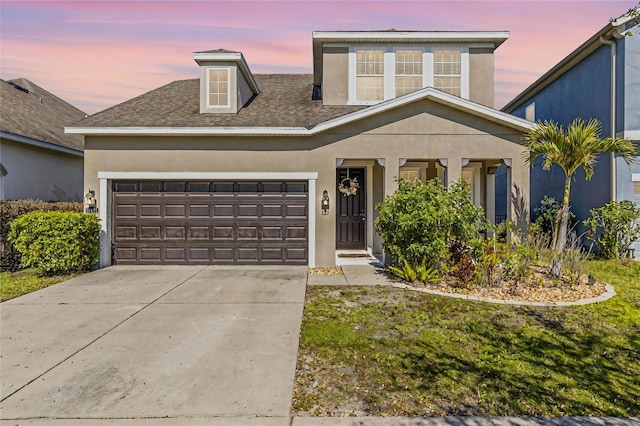 traditional home featuring a shingled roof, driveway, an attached garage, and stucco siding