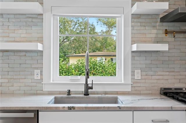 kitchen with light stone counters, a sink, stainless steel dishwasher, and white cabinets