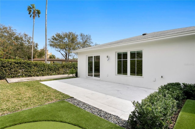 rear view of property featuring a patio, a yard, and stucco siding