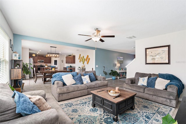 living room featuring ceiling fan with notable chandelier, visible vents, and baseboards