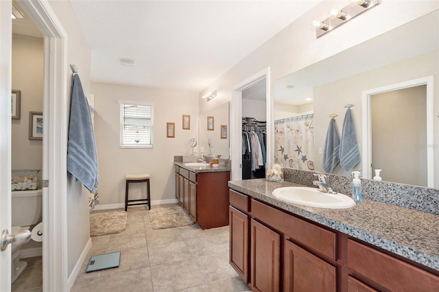 bathroom with two vanities, a spacious closet, toilet, a sink, and baseboards