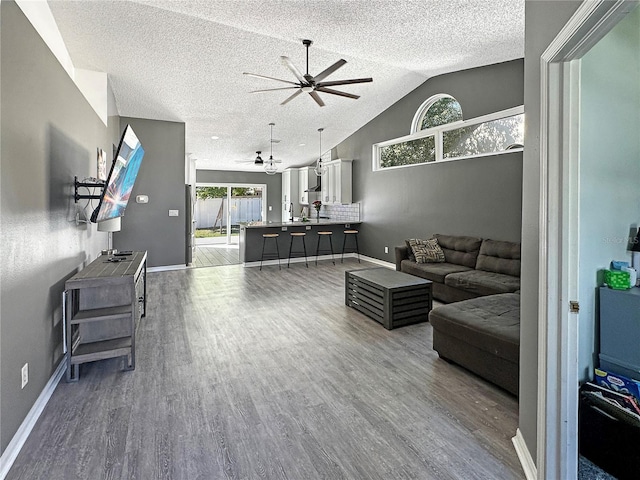 living area with ceiling fan, vaulted ceiling, a textured ceiling, and wood finished floors