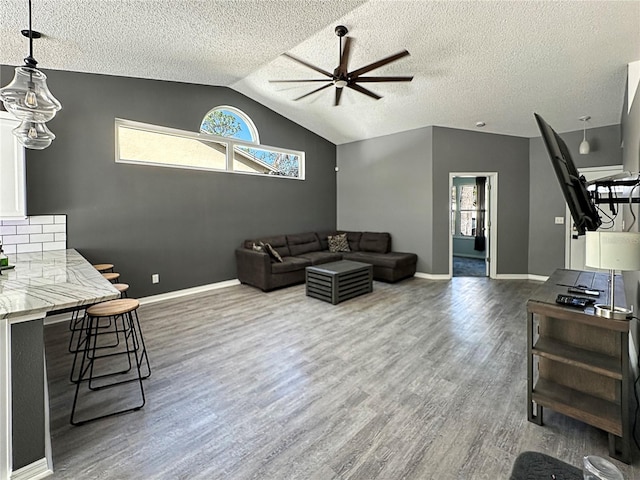 living area with baseboards, dark wood finished floors, ceiling fan, vaulted ceiling, and a textured ceiling