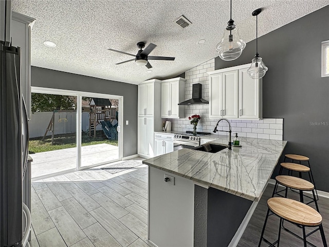 kitchen featuring light stone counters, a breakfast bar area, a sink, a peninsula, and wall chimney exhaust hood