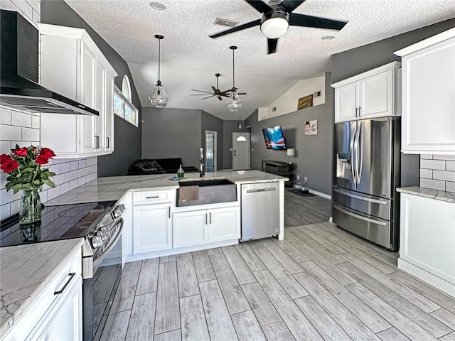 kitchen with white cabinets, appliances with stainless steel finishes, a peninsula, wall chimney range hood, and a sink