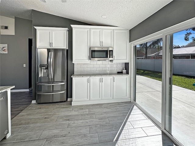 kitchen with lofted ceiling, stainless steel appliances, wood finish floors, white cabinetry, and backsplash