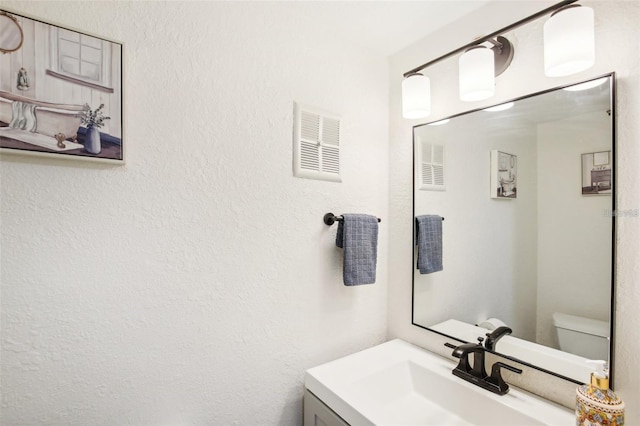 half bathroom featuring toilet, a textured wall, visible vents, and vanity