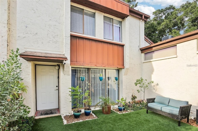 entrance to property featuring board and batten siding, a lawn, and stucco siding