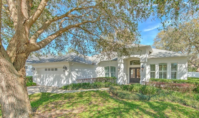 ranch-style house with a garage, stucco siding, concrete driveway, and french doors