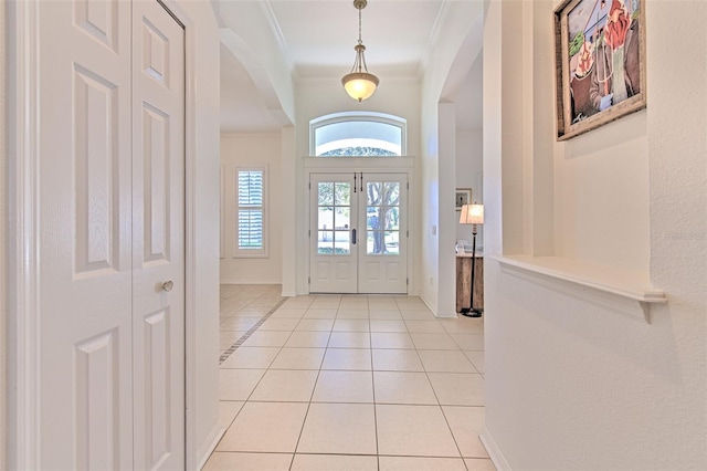 entrance foyer with light tile patterned floors, arched walkways, baseboards, french doors, and ornamental molding