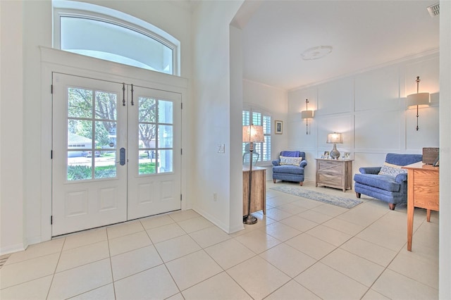 foyer entrance featuring visible vents, a decorative wall, crown molding, and light tile patterned flooring