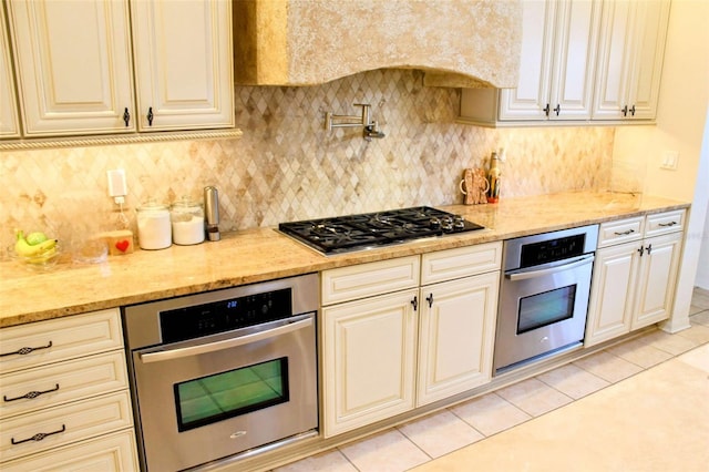 kitchen featuring appliances with stainless steel finishes, light tile patterned floors, cream cabinets, and light stone countertops