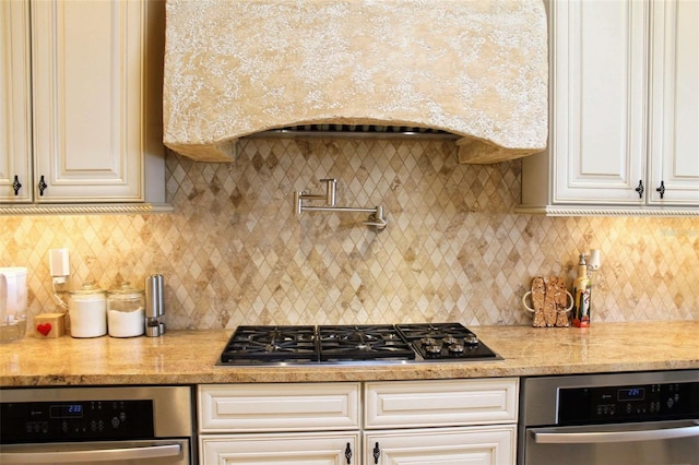 kitchen featuring stainless steel gas cooktop, light stone counters, backsplash, and oven